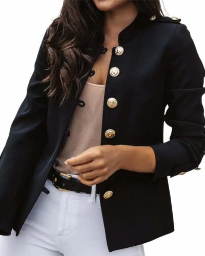 Photo d'une femme portant un blazer noir à col Mao et gros boutons dorés au style officier sur un top beige et un pantalon blanc ceinturé le tout sur fond blanc
