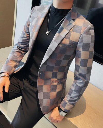 Un homme assis porte un blazer à grands carreaux gris, beige