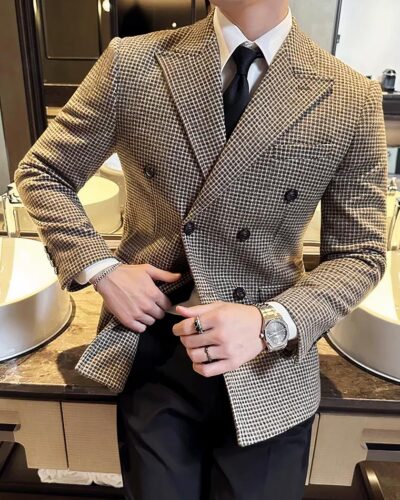 Homme portant un blazer à petits carreaux et étant adossé à un lavabo.