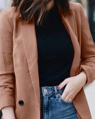 Photo d'un blazer vieux rose porté sur un jean bleu et un sous pull à col rond par une jeune femme dans un décor extérieur