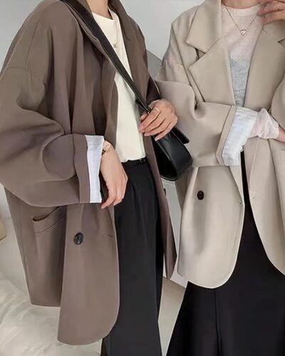 Photo de deux femmes debout portant chacune un blazer oversize très large l'un marron l'autre beige, ouverts sur des teeshirts blancs et bas noirs pantalon et jupe le tout sur un fond beige clair