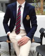 Un homme porte une veste bleue avec un écusson, chemise blanche et une cravatte rayée