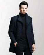 On voit un homme brun qui porte un manteau blazer noir très élégant et cintré.