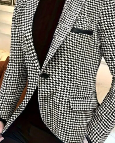 Un homme porte un blazer pied de poule noir et blanc, un pantalon et un pull à col roulé noirs