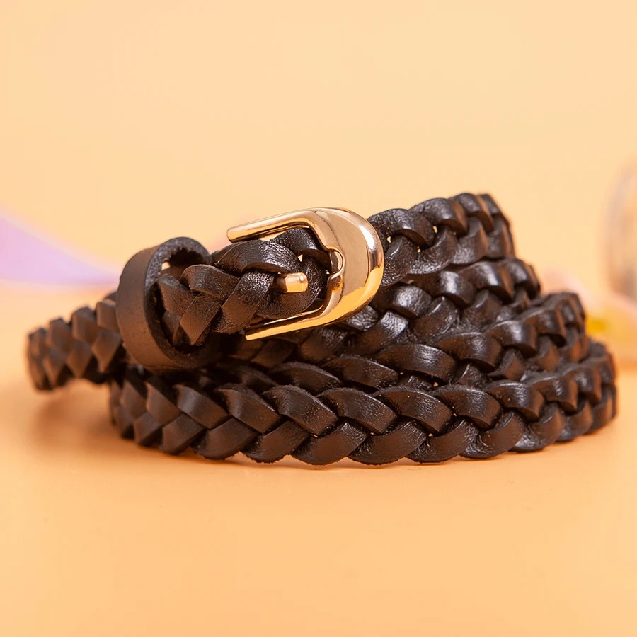 Ceinture fine tressée en cuir ceinture noire fine tressée avec une boucle dorée, enroulée sur elle-même, avec un fond orangé.