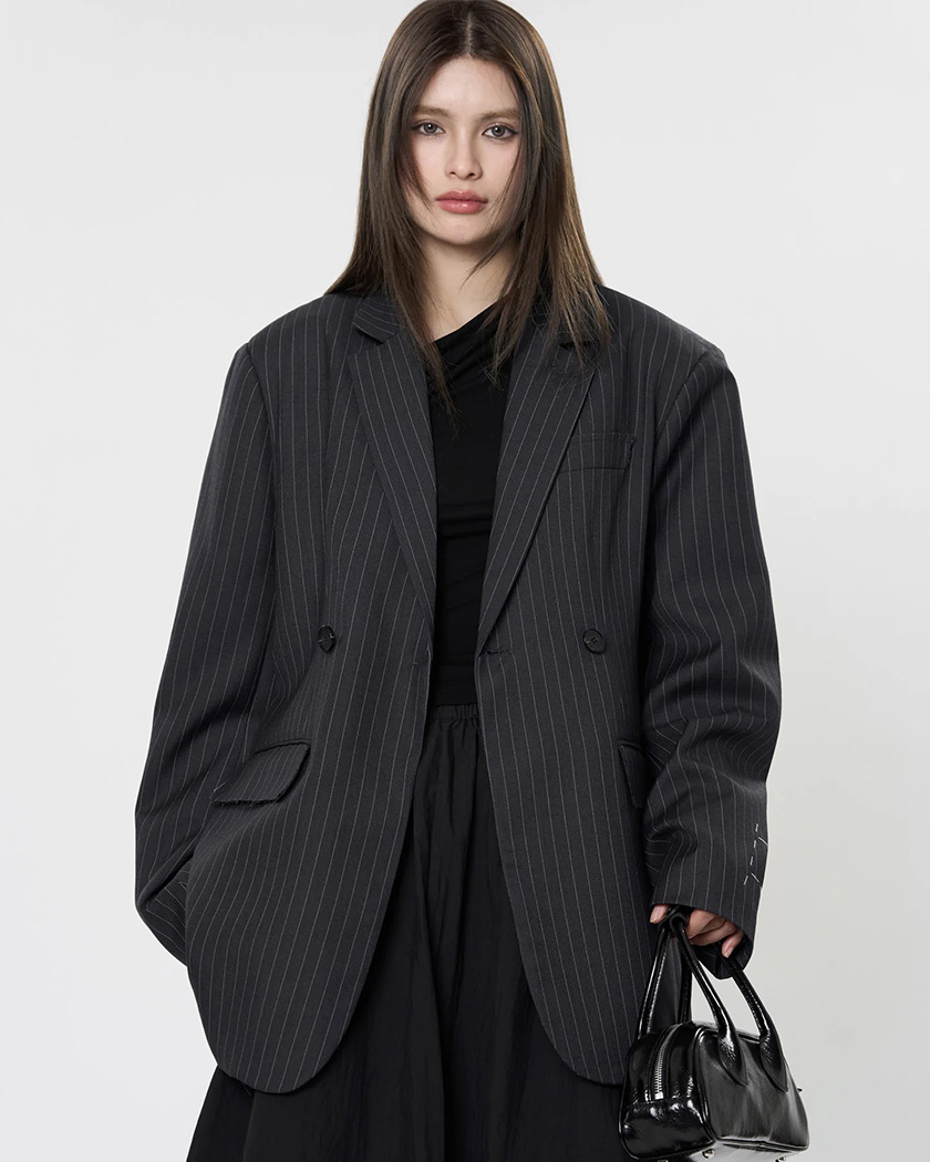 Femme caucasienne brune portant un blazer oversize à dos fendu pour femme sur un fond studio gris clair