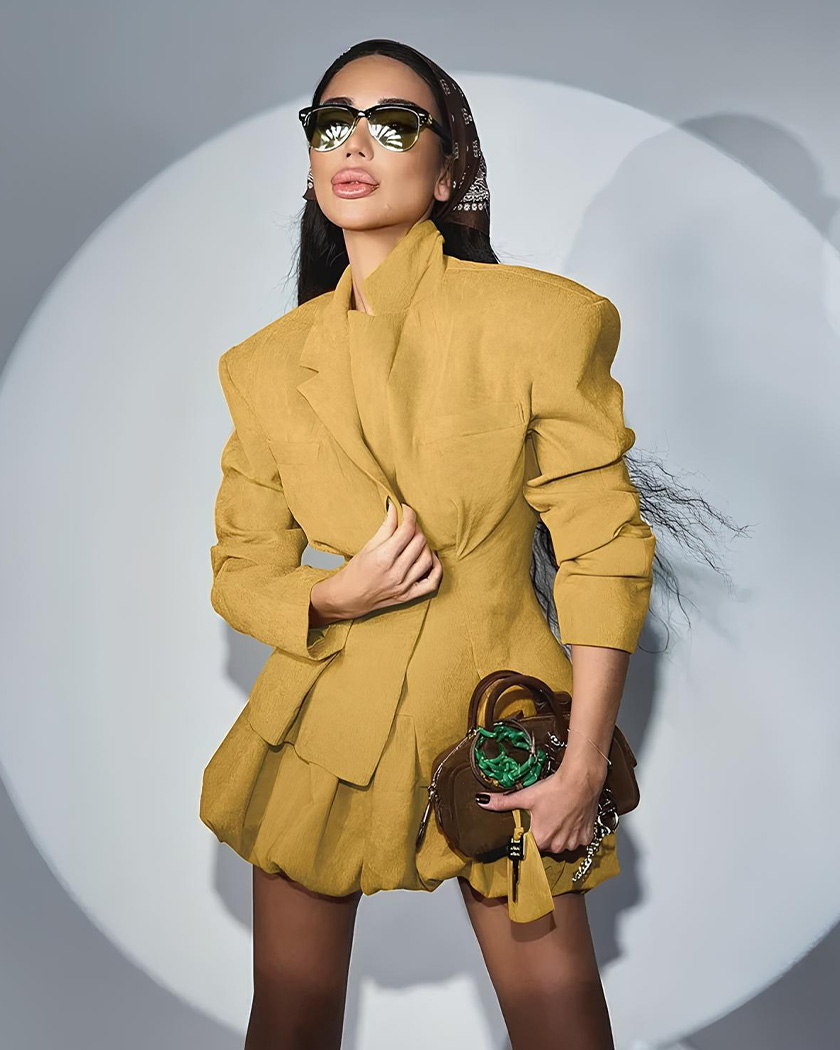 Femme brune portant un ensemble blazer jupe plissée taille haute sur un fond gris studio, éclairée par un spotlight