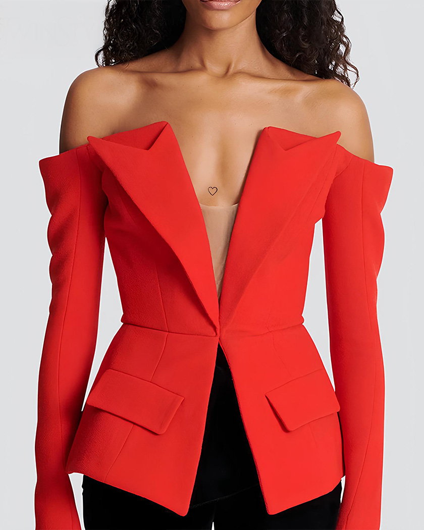 Femme brune portant un blazer ganté à manches bardot avec un pantalon noir sur fond blanc uni