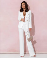 Femme brune portant un ensemble blazer pantalon taille haute blanc devant un mur rose