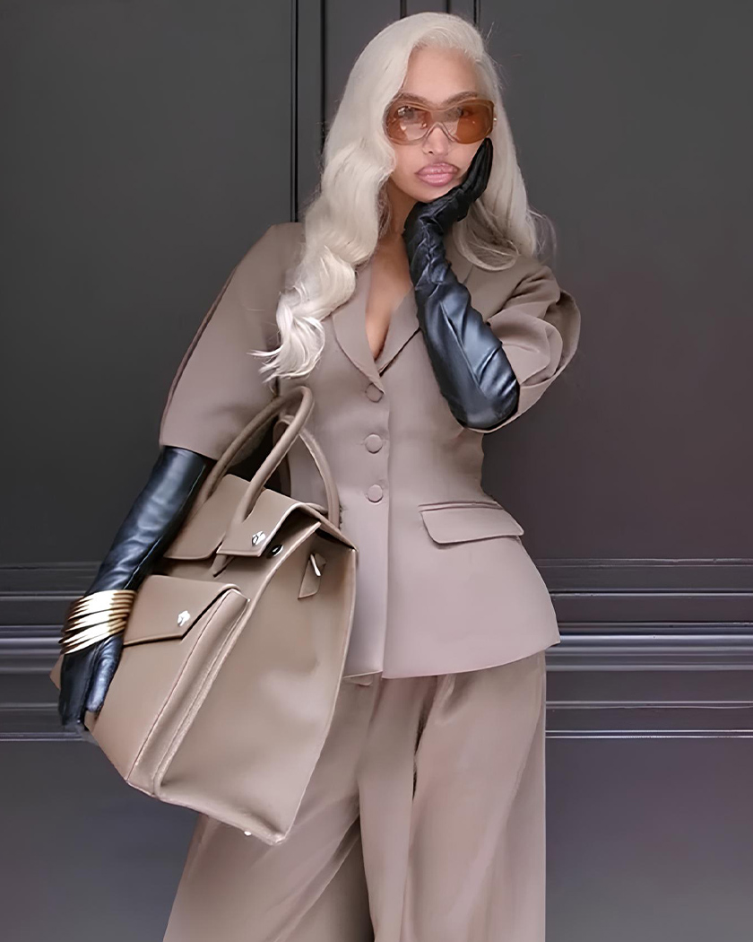 Femme noire à perruque blonde portant un ensemble blazer à manches courtes vintage face à un mur gris foncé